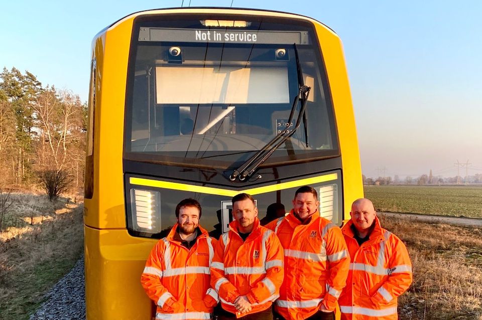 Four Metro drivers pose in front of new Stadler train on the test track at Brno