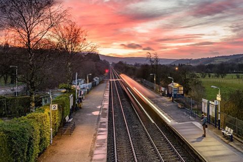 Sun setting in a red sky to the west, down the tracks at Bamford, a rural station in the Hope Valley