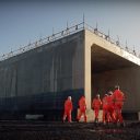 Engineers in orange suits in front of huge prefabricated concrete bridge