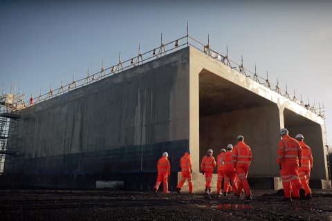 Engineers in orange suits in front of huge prefabricated concrete bridge