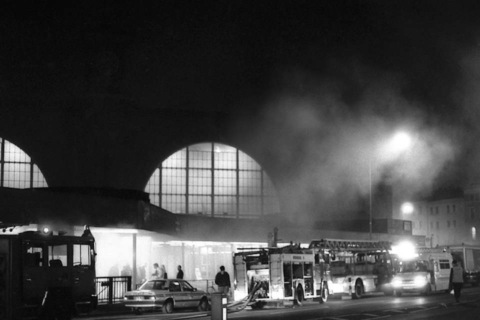 Black and white night time picture of the concourse in front of King's Cross station on the night of the fire underground in November 1987, with emergency services in attendance