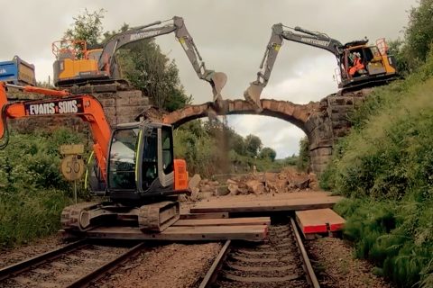 Two mechanical shovels work to demolish a bridge over a railway