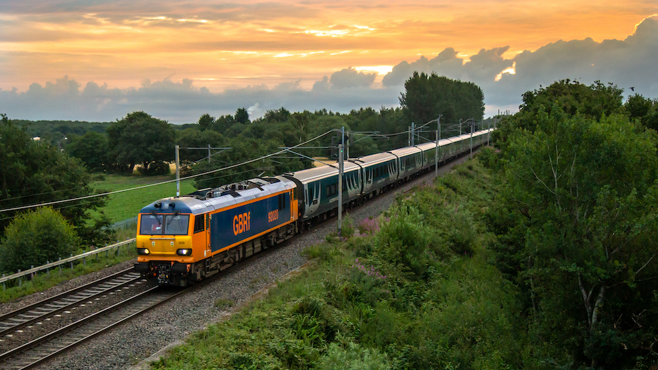 A class 92 GBRf loco hauls a Caledonian Sleeper train out of the sunset in a wooded setting