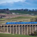 Blue liveried Lumo train of five cars on Lesbury Viaduct in Northumberland