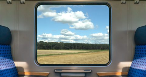 An empty blue seats on a german train with a window looking out on a corn field.