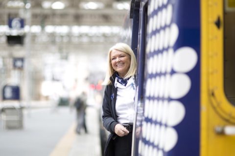 Smiling train conductor leans out of door of ScotRail train