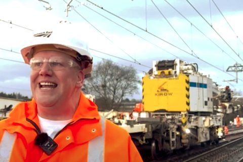 Candid portrait of a smiling Jemery Spence of Network Rail in orange coat in front of a yellow Kirow track crane