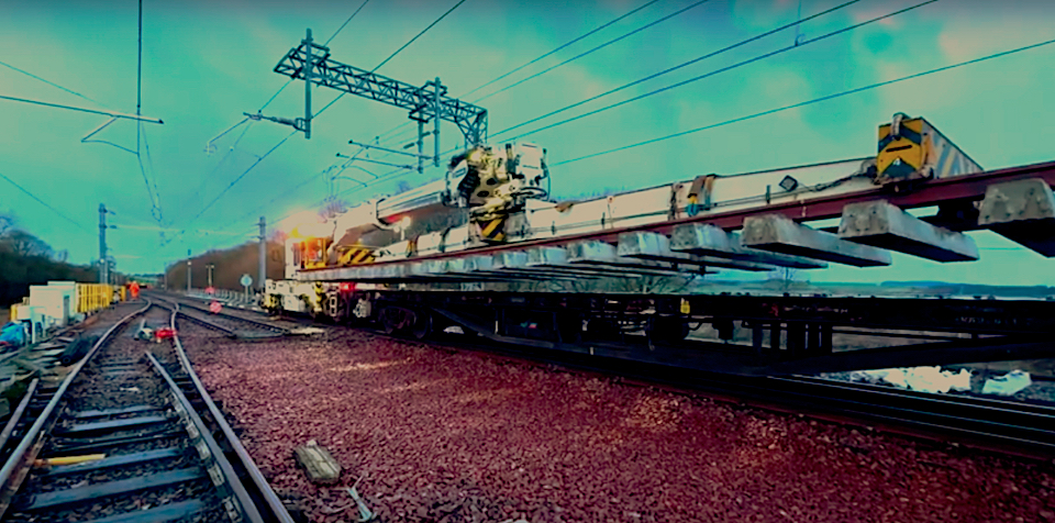 A track level view of a huge prefabricated track section being craned into place on top of red ballast